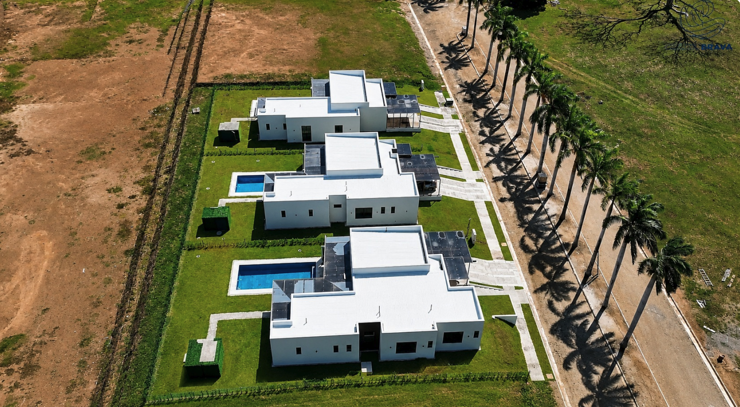 Aerial view of three completed villas with private pools and palm-lined street